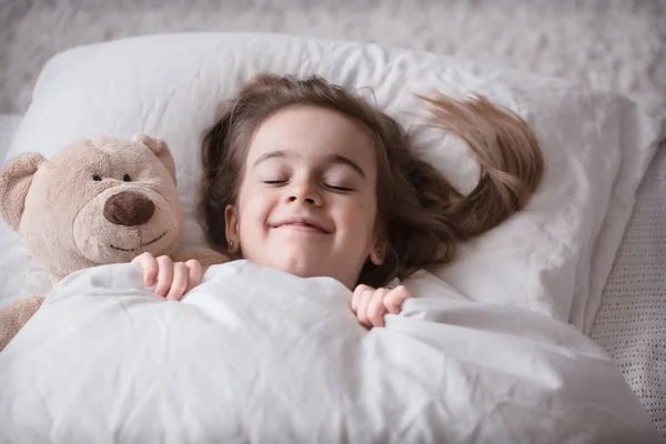 Oyuncak ile yatakta küçük sevimli kız — Stok fotoğraf