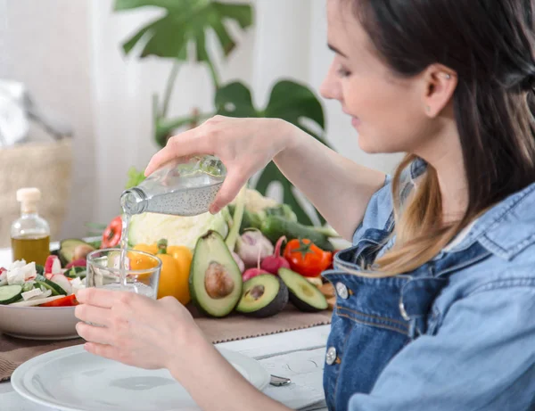 Junge Frau trinkt Wasser am Tisch mit Gemüse — Stockfoto