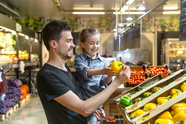 Happy family buys vegetables. Cheerful family of three choosing tomatoes in vegetable department of supermarket or market.