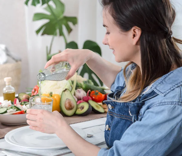 Junge Frau trinkt Wasser am Tisch mit Gemüse — Stockfoto