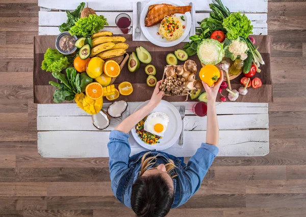 De vrouw aan de eettafel met biologisch eten, het uitzicht vanaf — Stockfoto