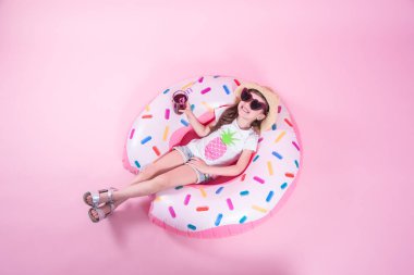 Küçük bir çocuk kız bir donut şişme daire üzerinde yatıyordu. Pembe arka plan. Üst te. Yaz konsepti.