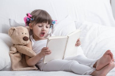 Sevimli küçük kız rahat beyaz bir yatakta yatarken gülümseyen