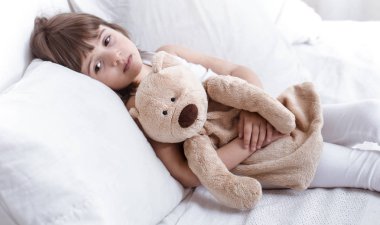 Sevimli küçük kız rahat beyaz bir yatakta yatarken gülümseyen