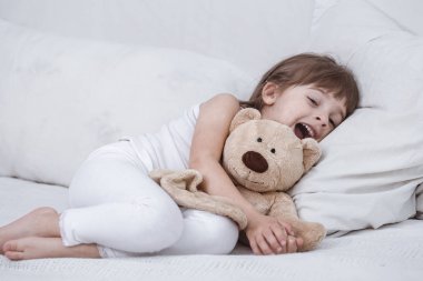 Sevimli küçük kız rahat beyaz bir yatakta yatarken gülümseyen