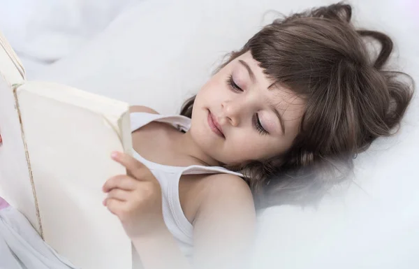 Linda niña sonriendo mientras está acostada en una acogedora cama blanca —  Fotos de Stock