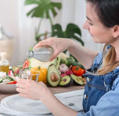 Sebzelerle masada su içen genç bir kadın.