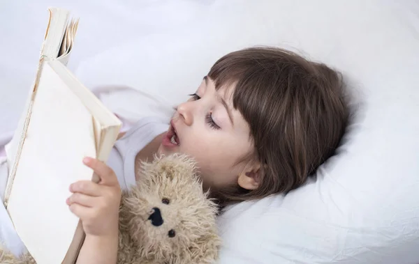 Süßes kleines Mädchen lächelt, während es in einem gemütlichen weißen Bett liegt — Stockfoto