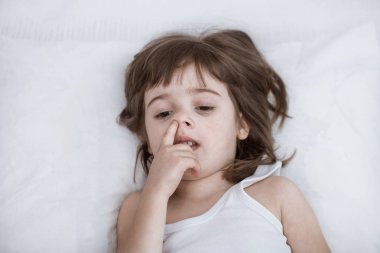 Sevimli küçük kız rahat beyaz bir yatakta yatarken gülümseyen