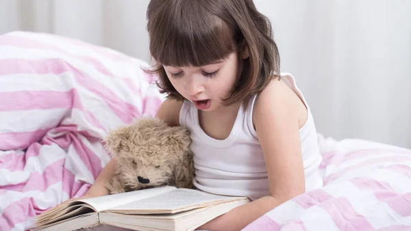 Linda niña sonriendo mientras está acostada en una acogedora cama blanca —  Fotos de Stock