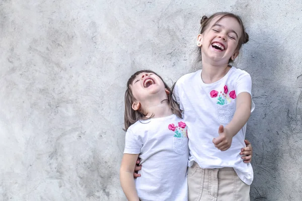 Χαρούμενα μικρά κορίτσια με γκρι υφή φόντο. Υπαίθριο πορτρέτο κοριτσάκι. Γκρίζο ανάγλυφο φόντο τοίχου. — Φωτογραφία Αρχείου