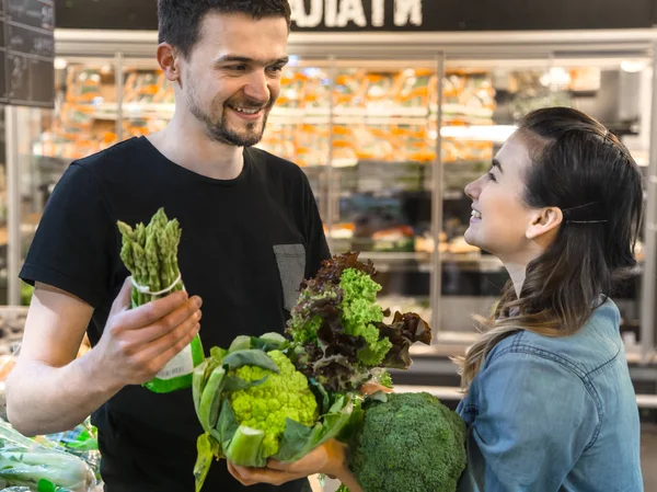 Happy family buys vegetables. Cheerful family of three choosing tomatoes in vegetable department of supermarket or market.