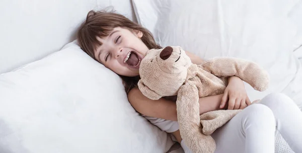 Cute little girl smiling while lying in a cozy white bed — Stock Photo, Image