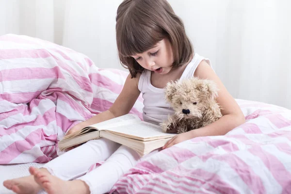 Linda niña sonriendo mientras está acostada en una acogedora cama blanca —  Fotos de Stock