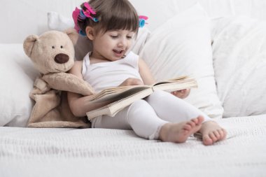 Sevimli küçük kız rahat beyaz bir yatakta yatarken gülümseyen