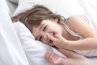 Sevimli küçük kız rahat beyaz bir yatakta yatarken gülümseyen