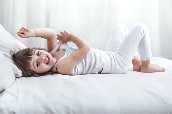 Carino bambina sorridente mentre si trova in un accogliente letto bianco — Foto Stock