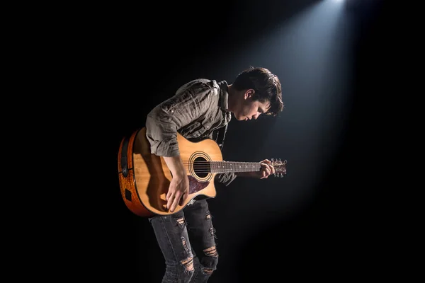 Guitarist, music. A young man plays an acoustic guitar on a blac