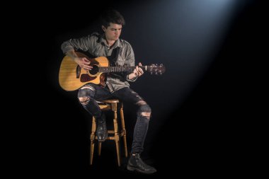 akustik gitar çalan müzisyen, mama sandalyesinde oturan, güzel yumuşak ışık ile siyah arka plan