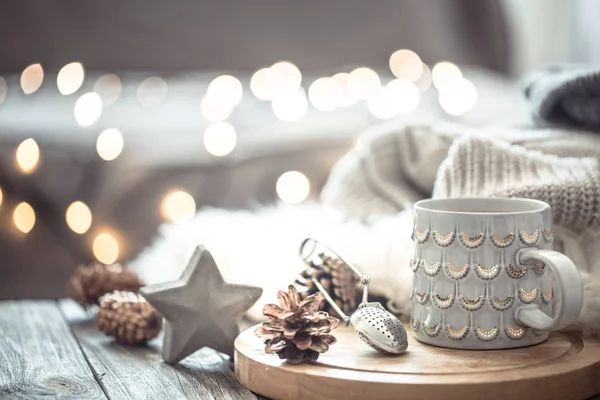 Coffee cup over Christmas lights bokeh in home on wooden table with sweater on a background and decorations. Holiday decoration, magic Christmas