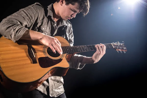 Guitarrista, música. Um jovem toca guitarra acústica num blac — Fotografia de Stock