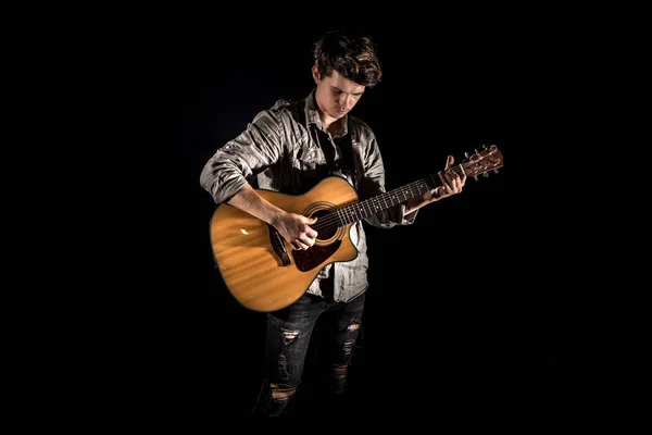 Guitarist, music. A young man plays an acoustic guitar on a blac