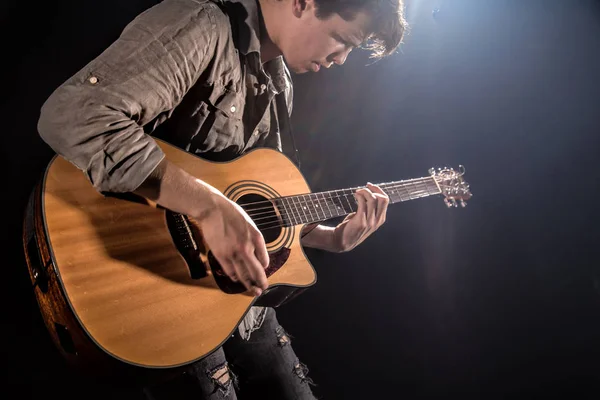 Guitarrista, música. Um jovem toca guitarra acústica num blac — Fotografia de Stock