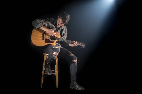 musician playing acoustic guitar, sitting on high chair, black b