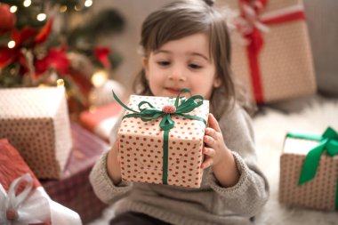 Sevimli küçük kız bir hediye kutusu tutarak ve onun yatağında onun odasına evde otururken gülümseyen