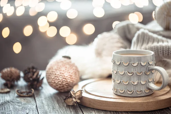 Φλιτζάνι καφέ πάνω από τα Χριστουγεννιάτικα φωτάκια bokeh στο σπίτι σε ξύλινο τραπέζι με πουλόβερ σε φόντο και διακοσμητικά. Διακόσμηση διακοπών, μαγικά Χριστούγεννα — Φωτογραφία Αρχείου