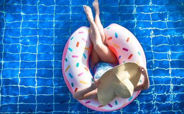 Şapkalı bir kadın havuzda şişme bir daire üzerinde rahatlatır.