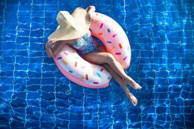 Şapkalı bir kadın havuzda şişme bir daire üzerinde rahatlatır.