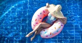 Žena v klobouku relaxuje na nafučitelné kružnici v bazénu.