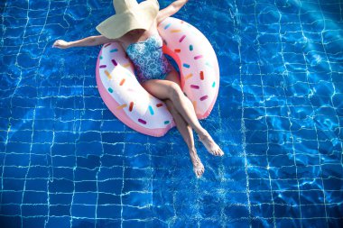 Şapkalı bir kadın havuzda şişme bir daire üzerinde rahatlatır.