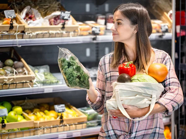 Genç bir kız mağazameyve ve sebze seçer ve koyar — Stok fotoğraf