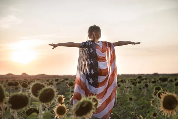 Ein Mädchen hält bei Sonnenuntergang eine amerikanische Flagge in der Hand . — Stockfoto