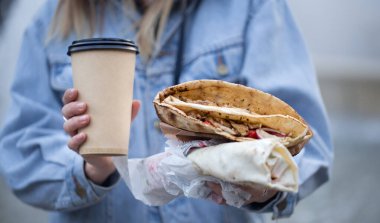 Elinde bir bardak kahve ve fast food tutan genç bir kadın..