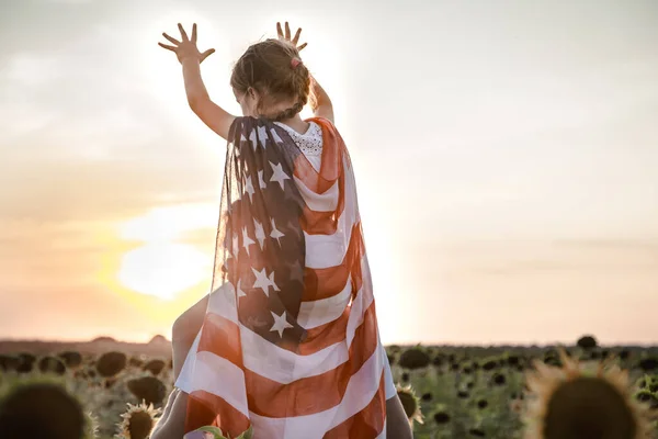 Ein Mädchen hält bei Sonnenuntergang eine amerikanische Flagge in der Hand . — Stockfoto