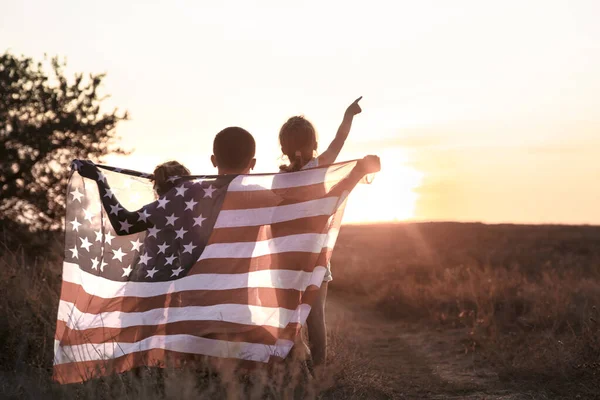 Eine glückliche Familie mit einer amerikanischen Flagge bei Sonnenuntergang. — Stockfoto