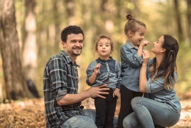Genç bir aile sonbahar ormanında çocuklarla yürüyor..