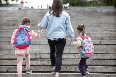 İlkokulun ebeveynleri ve öğrencileri el ele gider. Sırt çantalı iki kızın annesi. Dersler başlıyor. Sonbaharın ilk günü.