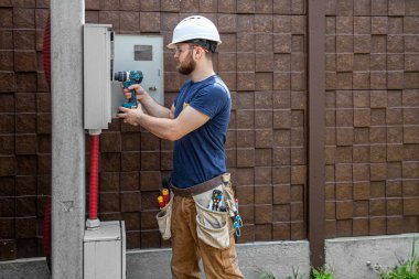 Elektrikçi İnşaatçı, bir sanayi santralinin gövdesindeki elektrik hattındaki kablo bağlantısını inceliyor. Elektrikçi aletli profesyonel bir işçi. Profesyonel olarak çalışma kavramı..