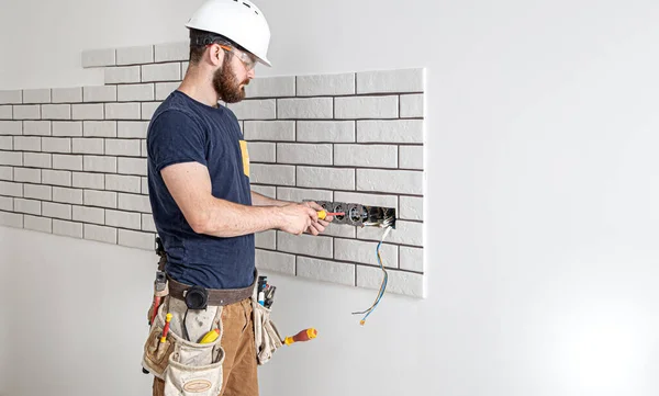 Electrician Builder at work, installation of sockets and switches. Professional in overalls with an electrician\'s tool. Against the background of the repair site. The concept of working as a professional.