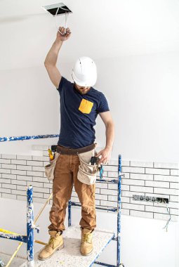 Elektrik İmalathanesi, yükseklerde lamba montajı. Profesyonel, tulumlu ve elektrikli aletli. Tamir alanının arka planında. Profesyonel olarak çalışma kavramı..