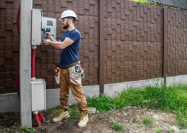 Elektrikçi İnşaatçı, bir sanayi santralinin gövdesindeki elektrik hattındaki kablo bağlantısını inceliyor. Elektrikçi aletli profesyonel bir işçi. Profesyonel olarak çalışma kavramı..