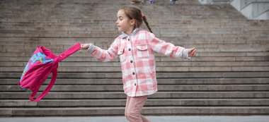 Evrak çantalı liseli kıza. Derslerin başlangıcı ve sonbaharın ilk günü. Tatlı bir kız geniş bir merdivenin arka planında duruyor.