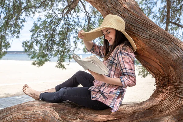 A happy girl reads a book on a tree, against the background of a sea beach. The person abstracted from everything. The concept of relaxation and tranquility.