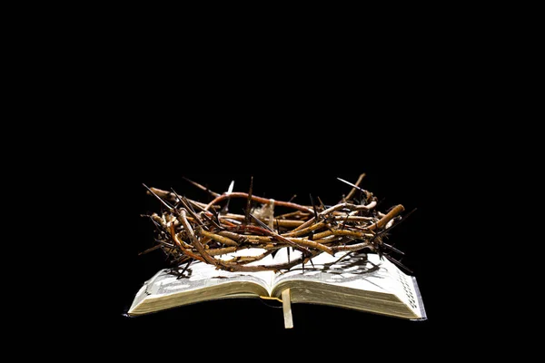 The crown of thorns lies on the open book of the Bible. Objects on an isolated black background. The concept of Holy week.