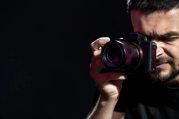 The person is holding a camera and is set up for shooting. The photographer looks into the camera\'s viewfinder and takes pictures. Object on a black background. Space for text.