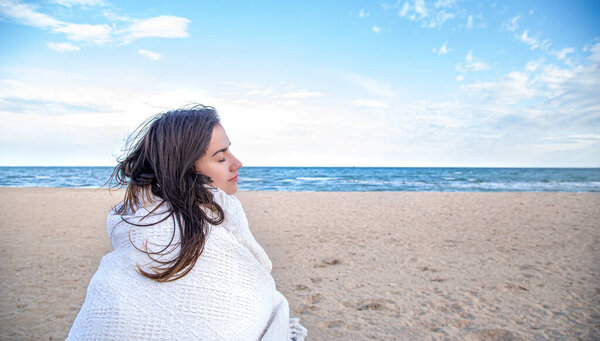 A young woman by the sea covered with a cozy blanket .